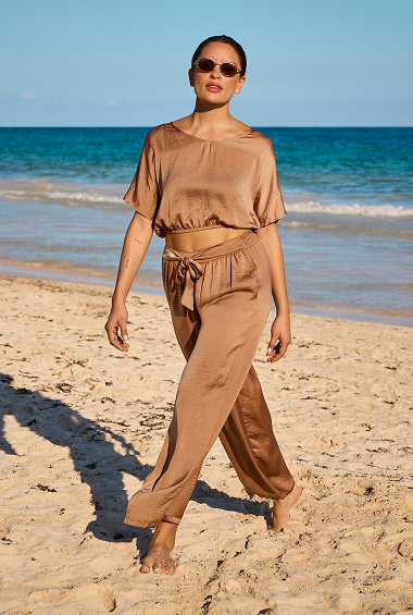 Woman walking on the beach and wearing a beige satin top and pants from the brand Santemare. 
