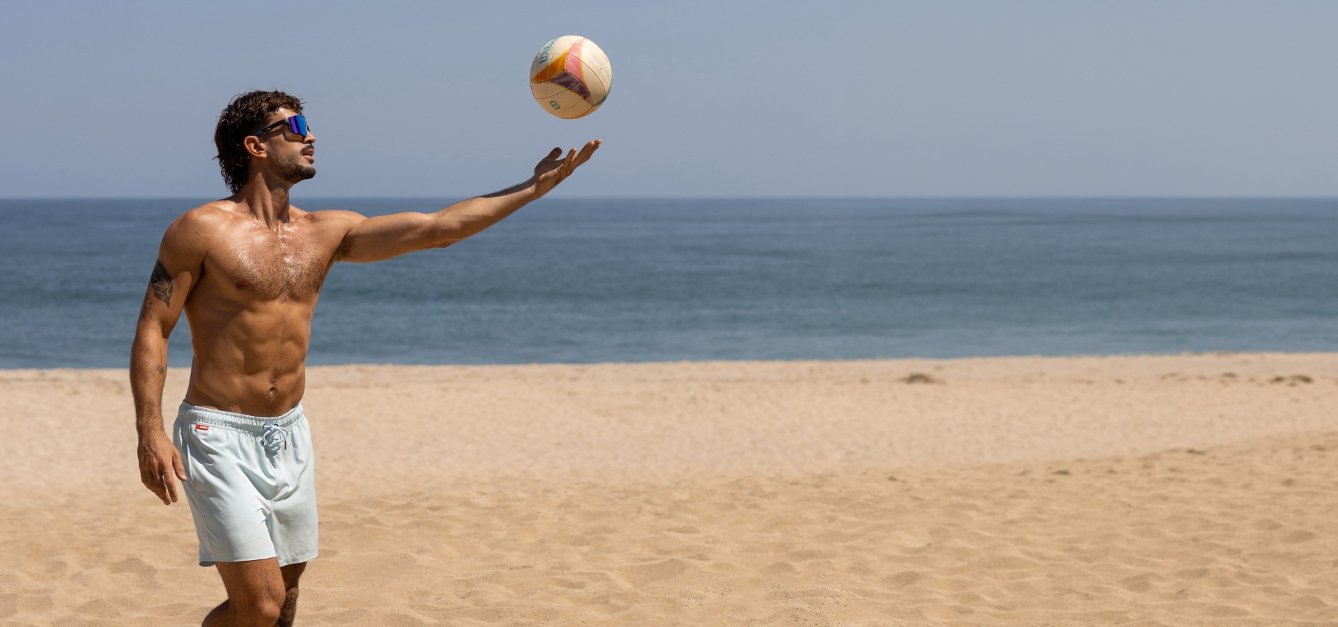 Man on a beach playing with a ball and wearing blue volleyball shorts from the brand Hamabe.