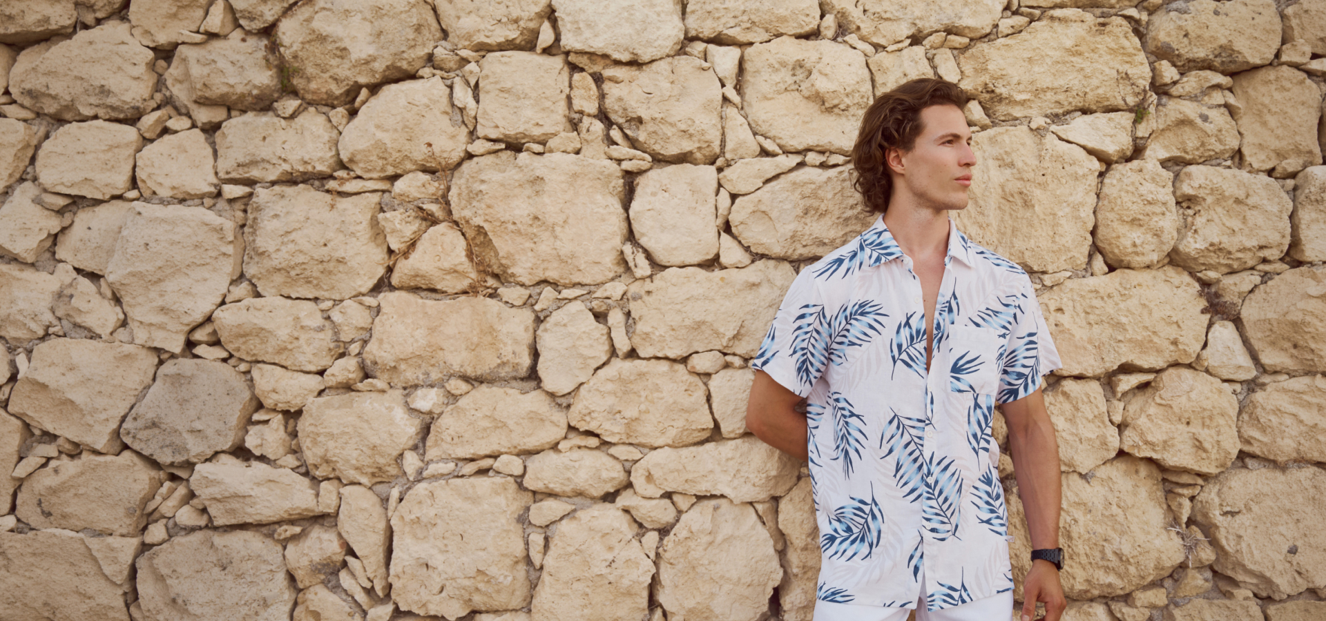 A man standing against a rock wall, wearing an Off The Beach linen outfit.	