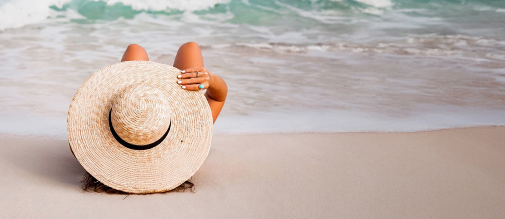 A woman lying on the beach wearing a sun hat. 