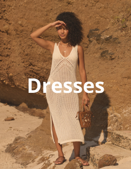 Woman wearing a long crochet dress from the My Bikini Story brand, standing gracefully on the sand under the sun. 