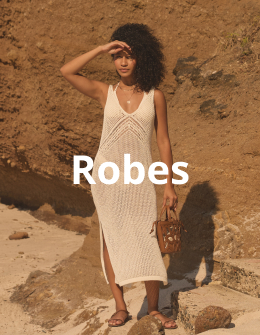 Femme portant une longue robe en crochet de la marque My Bikini Story, debout avec élégance sur le sable sous le soleil.