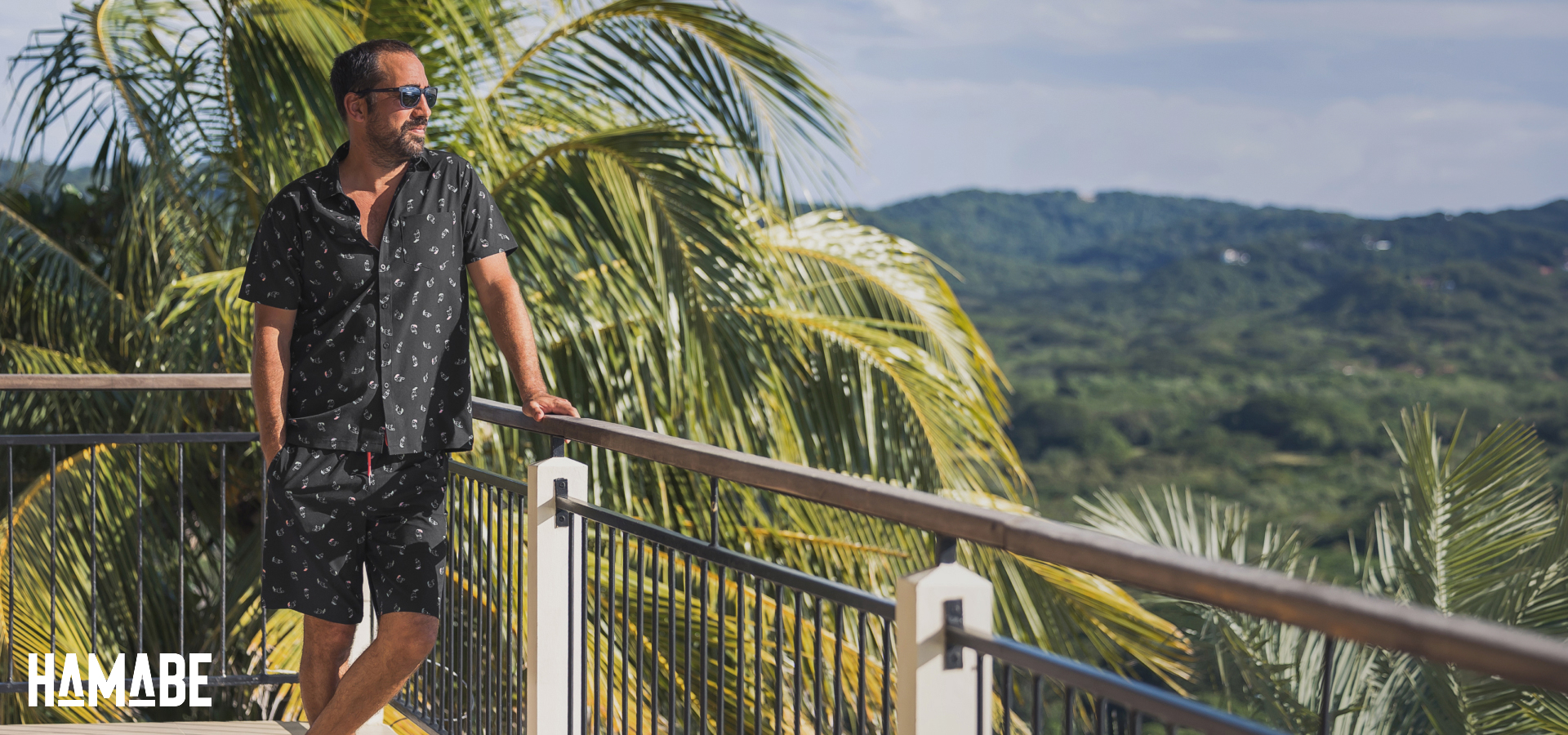 Un homme se tenant sur la rembarde d&rsquo;un balcon et regardant la vue en portant un ensemble assorti d&rsquo;Hamabe. 