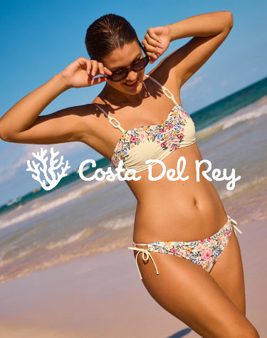 Woman walking on the beach and holding her sunglasses, wearing a floral bikini set from Costa Del Rey.