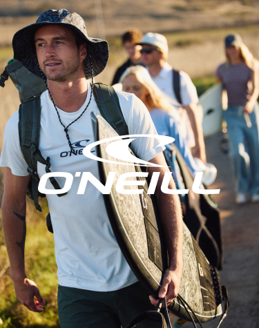 A man walking with a group, holding a surfboard, and wearing a T-shirt and swim trunks from the brand O&rsquo;Neill.