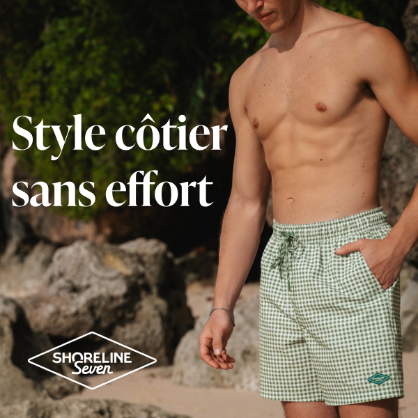 Homme sur la plage avec une main dans la poche d&rsquo;un maillot au motif &agrave; carreaux vert et blanc de la marque Shoreline Seven. 