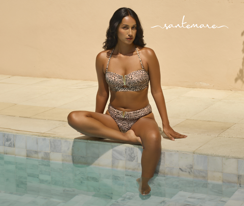 Woman sitting by the edge of a pool, wearing a leopard-print bikini set from Santemare.