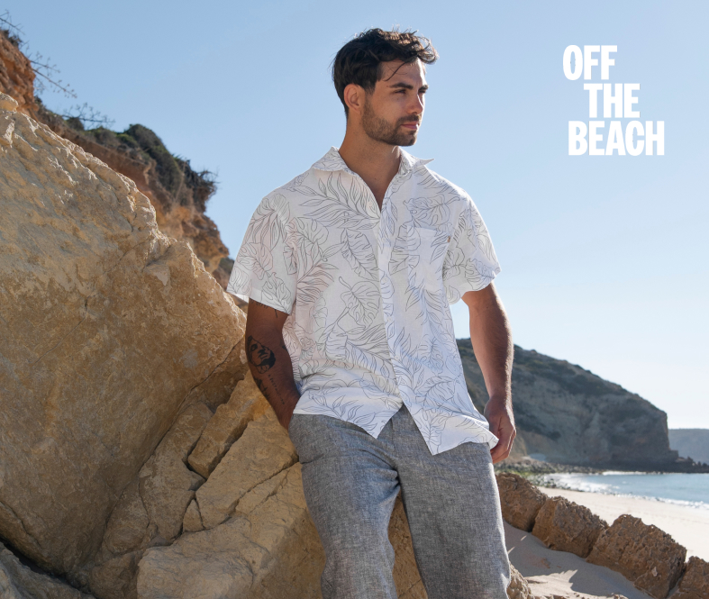 Man leaning against a rock, wearing a linen shirt and pants set from Off The Beach.