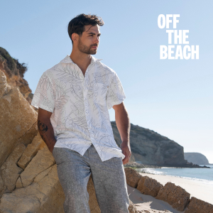 Man leaning against a rock, wearing a linen shirt and pants set from Off The Beach.