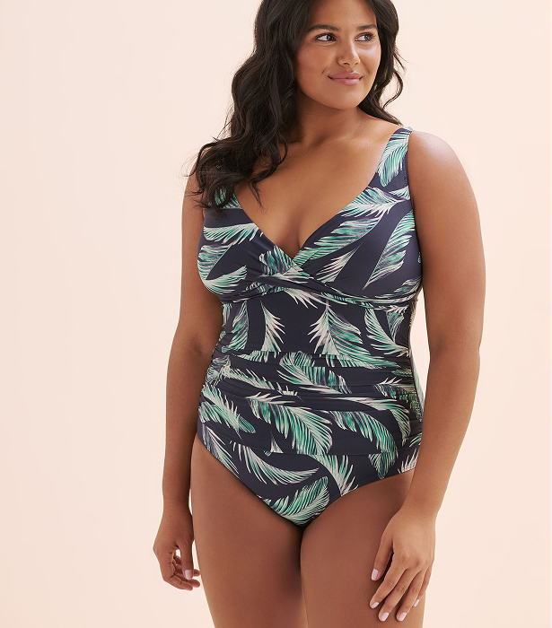 Woman wearing a leaf‑print one‑piece swimsuit by the brand Artesands. 