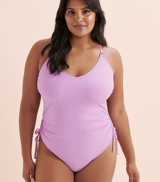 Woman wearing a purple one‑piece swimsuit by the brand Tropik. 