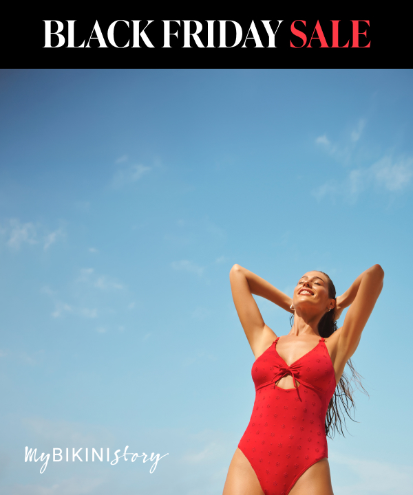A woman standing against a backdrop of the sky, wearing a red one-piece swimsuit, with her hands running through her wet hair.	