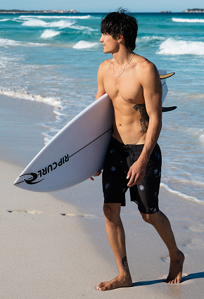 Man on the beach holding a surfboard and wearing minimalist-pattern Billabong boardshorts.	