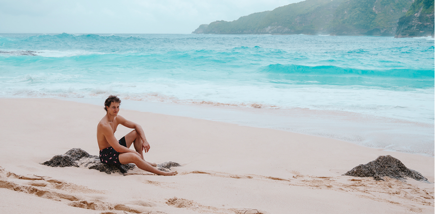 Homme assis sur une plage et portant un maillot de bain noir de la marque Hamabe.