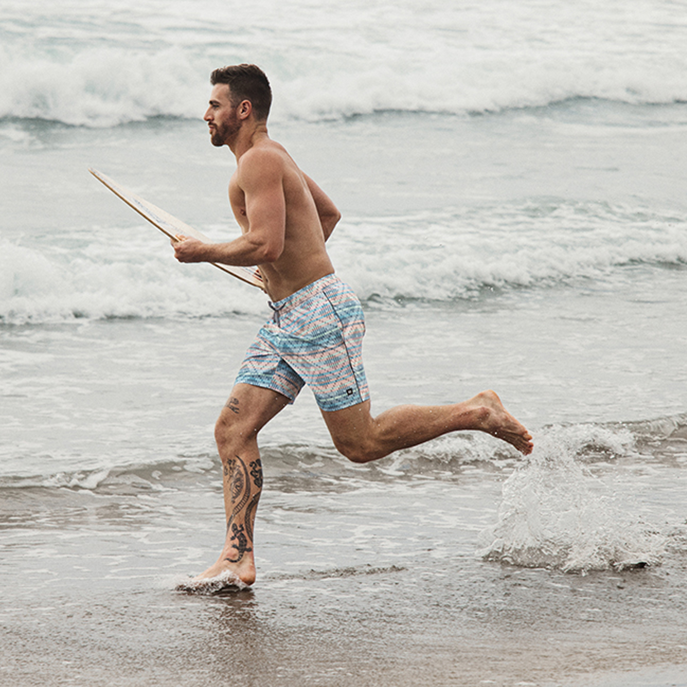 Man running towards the sea with a surf board, wearing a Saxx geometric swimsuit – Bikini  Village