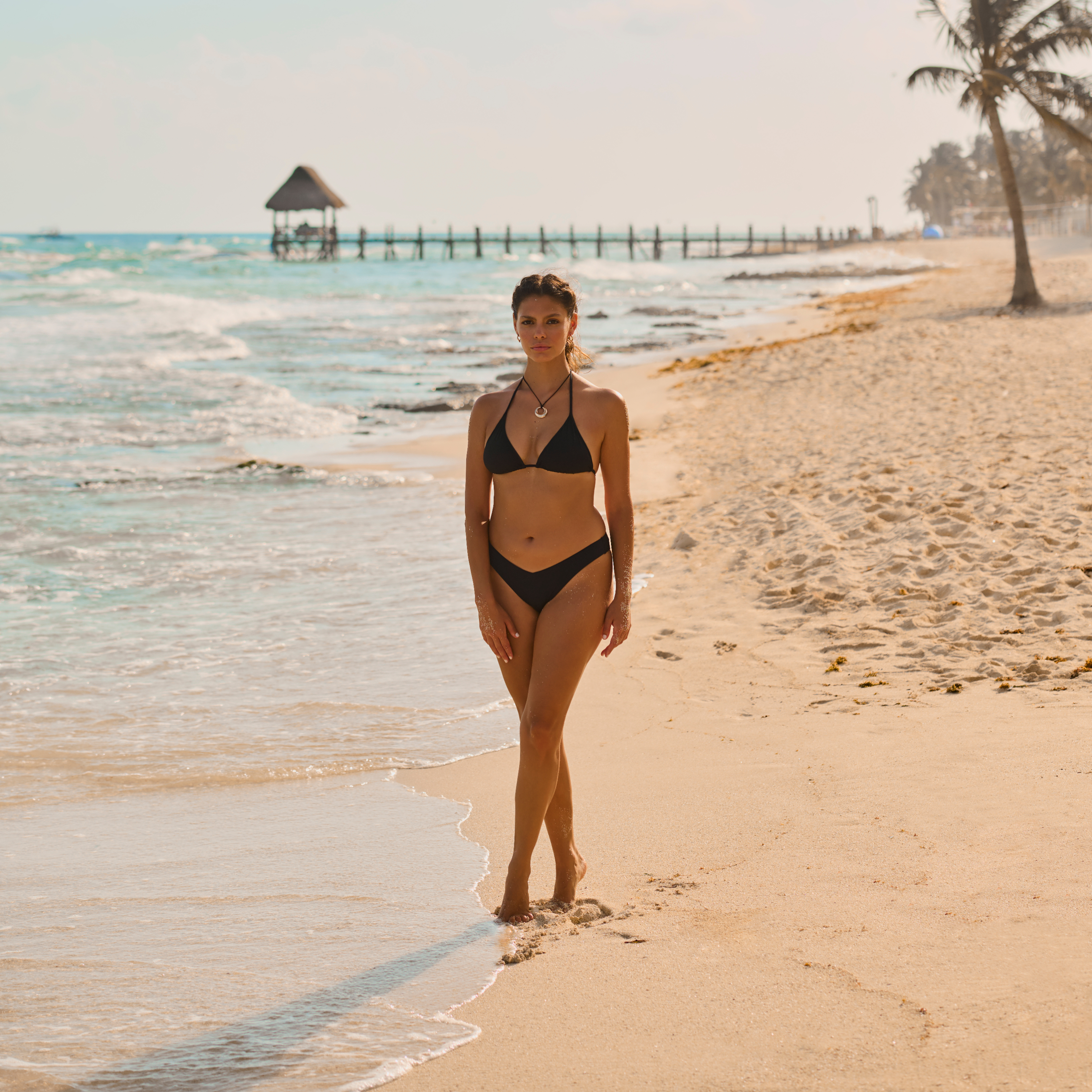 A woman walking on the beach in a black bikini